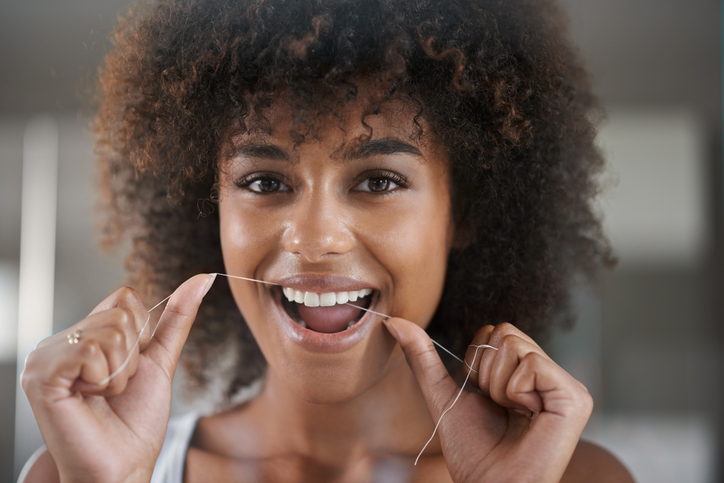 Shot of a young woman flossing her teeth in the mirror