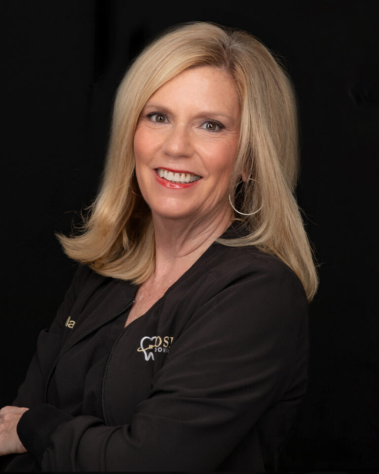 Margaret, a woman with shoulder-length hair in black scrubs, stands against a black background.