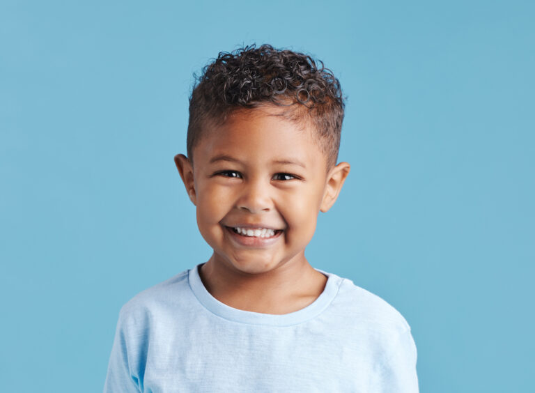 Portrait Of A Smiling Little Brown Haired Boy Looking At The Camera. Happy Kid With Good Healthy Teeth For Dental On Blue Background