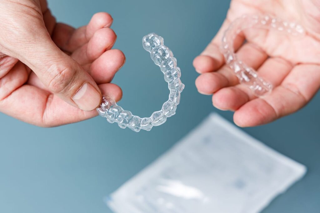 Close up of an Invisalign invisible aligner being held by a pair of hands