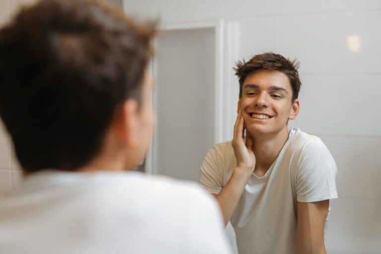 Teen in a white tee examining his smile in the mirror