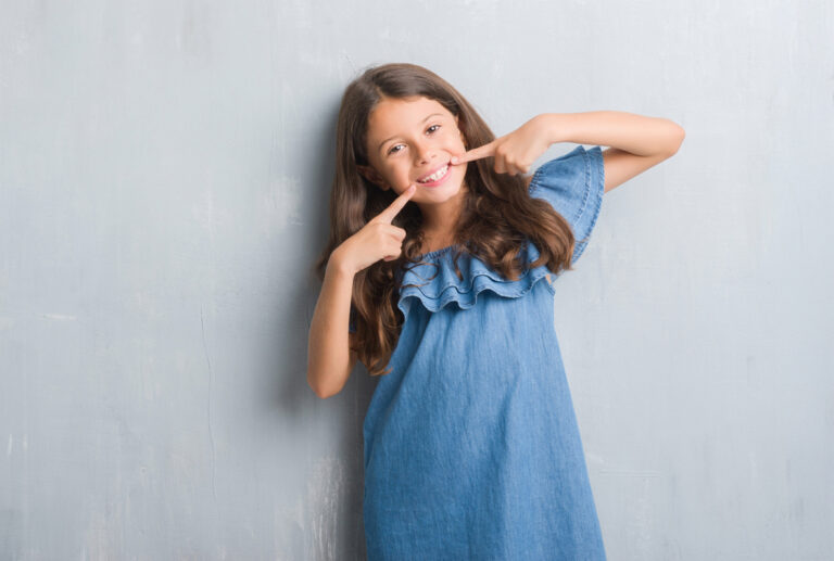 Young hispanic kid over grunge grey wall smiling confident showing and pointing with fingers teeth and mouth.